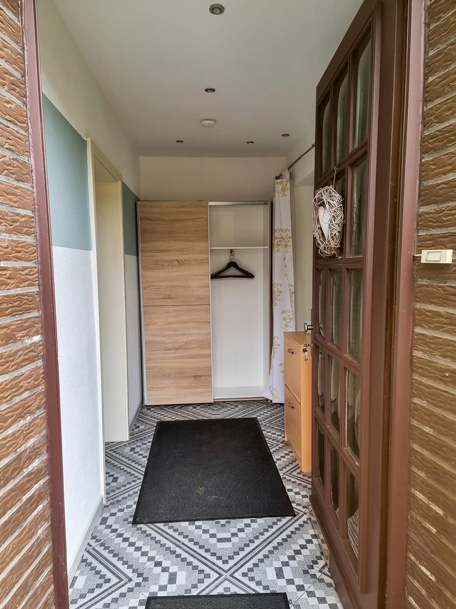 Blick durch die offene Haustür in den Flur mit Schiebetürenschrank, Garderobe und gemustertem Fliesenboden